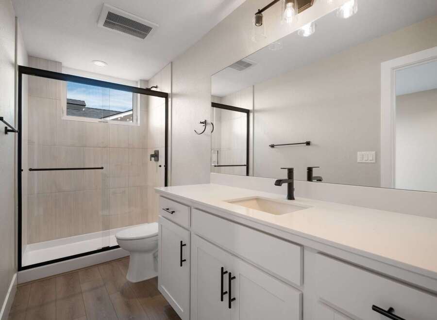 This modern bathroom features a sleek white vanity with black hardware, complemented by a spacious walk-in shower with a glass enclosure and light-toned tile.