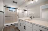 This modern bathroom features a sleek white vanity with black hardware, complemented by a spacious walk-in shower with a glass enclosure and light-toned tile.