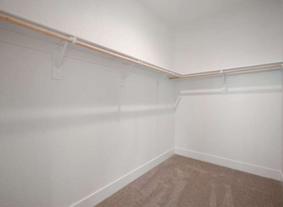 This spacious walk-in closet offers ample storage with multiple wooden hanging rods and white shelving brackets.