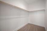 This spacious walk-in closet offers ample storage with multiple wooden hanging rods and white shelving brackets.