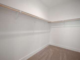 This spacious walk-in closet offers ample storage with multiple wooden hanging rods and white shelving brackets.