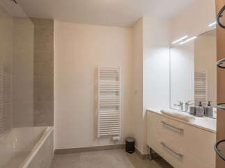 This modern bathroom features a sleek white vanity with ample drawer space and a large mirror illuminated by modern lighting.