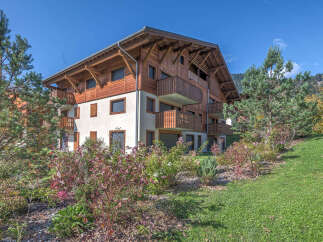 Experience alpine living in this stunning wooden chalet-style apartment building, nestled amidst lush greenery and rolling hills.