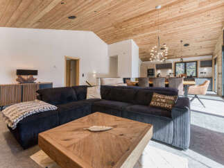 Experience modern mountain living in this stunning open-concept living space, featuring a cozy sectional sofa, a rustic wooden coffee table, and a sleek, integrated kitchen perfect for entertaining.