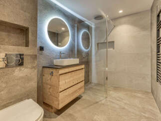 Experience modern luxury in this stunning bathroom, featuring a sleek vanity with a vessel sink and a backlit round mirror.