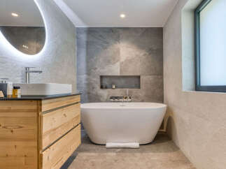Experience luxury in this modern bathroom featuring a freestanding soaking tub and a sleek vessel sink atop a natural wood vanity.