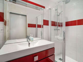 This modern bathroom features a sleek white vanity with a red cabinet, complemented by a large mirror and a spacious glass-enclosed shower.