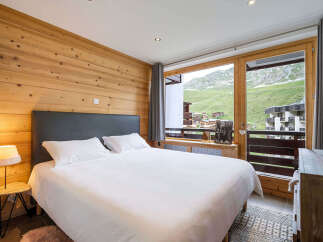 Experience breathtaking mountain views from this charming bedroom, featuring a cozy bed and a rustic wooden accent wall.