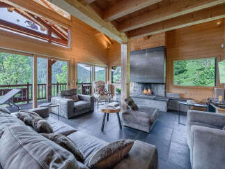 Experience luxury mountain living in this stunning wooden chalet, featuring a grand stone fireplace and expansive windows offering breathtaking panoramic views of the surrounding forest and valley.