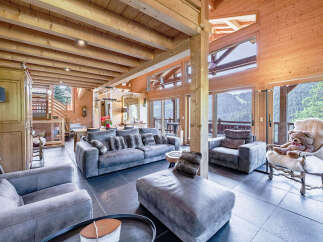 Experience luxurious mountain living in this stunning chalet, featuring a spacious open-plan living area with plush grey sofas and a cozy chaise lounge.