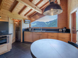 Experience breathtaking mountain views from this charming wooden kitchen, featuring a large triangular window that frames the stunning alpine scenery.
