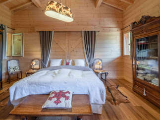 Experience rustic charm in this cozy wooden bedroom, featuring a plush king-sized bed adorned with decorative pillows and a soft, textured throw.