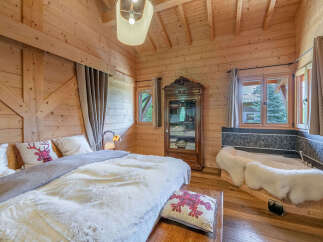 Experience rustic luxury in this charming log cabin bedroom, featuring a plush bed adorned with festive pillows and a cozy white duvet.