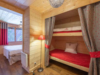 Experience cozy mountain living in this charming wooden cabin featuring a comfortable bunk bed nook with red bedding and playful checkered curtains.