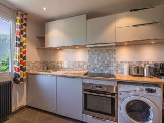This modern kitchen features sleek grey cabinetry, a built-in oven, and a stovetop, complemented by a stylish tiled backsplash.