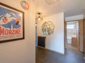 Step into a charming hallway featuring a vintage ski poster of Morzine, a unique circular mirror, and a modern black radiator.