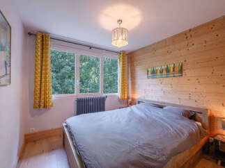 Experience cozy mountain living in this charming bedroom featuring warm, wood-paneled walls and a large window offering serene forest views.