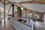Experience luxury mountain living in this stunning open-plan chalet, featuring a modern kitchen island with a built-in cooktop, a grand stone fireplace, and a spacious dining area.