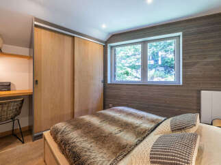 Experience cozy mountain living in this charming bedroom featuring a plush fur throw on the bed and a convenient built-in desk with a wicker chair.