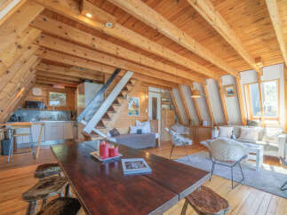 Experience rustic charm in this A-frame cabin featuring a cozy living area with a fireplace and ample natural light.