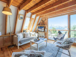 Experience breathtaking mountain views from this charming alpine living room, featuring a cozy sofa, a modern coffee table, and a large sliding glass door that opens to a scenic balcony.