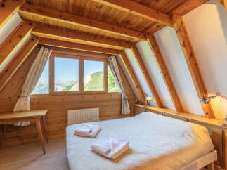Experience breathtaking mountain views from this charming attic bedroom, featuring a cozy bed adorned with fresh white towels and a rustic wooden desk.