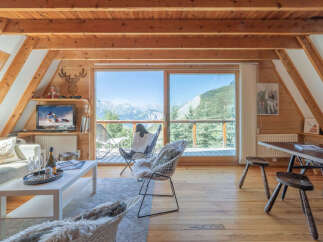 Experience breathtaking mountain views from this charming chalet living room, featuring a cozy seating area and a large sliding glass door that opens to a scenic balcony.