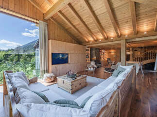 Experience luxury mountain living in this stunning wooden chalet, featuring a spacious open-plan living area with a large sectional sofa and a cozy fireplace.