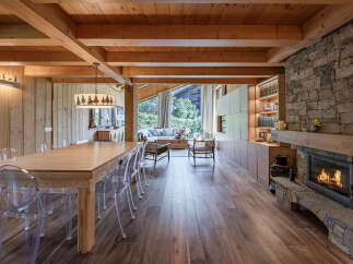 Experience rustic luxury in this stunning mountain retreat, featuring a grand wooden dining table with modern clear chairs, perfect for family gatherings.