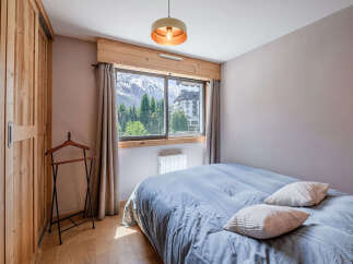 Experience breathtaking mountain views from this charming bedroom, featuring a cozy double bed with plush pillows and a large window overlooking snow-capped peaks and lush greenery.