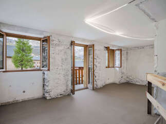Discover this unfinished interior space with rustic stone walls and large wooden-framed windows offering stunning mountain views.