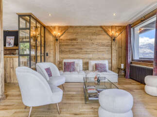 Experience luxury mountain living in this stunning chalet living room, featuring a cozy seating area with plush white armchairs and a modular sofa adorned with decorative pillows.