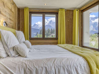 Experience breathtaking mountain views from this cozy bedroom, featuring a comfortable bed adorned with plush pillows and a vibrant yellow throw.