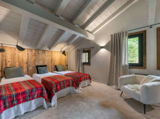 Experience cozy mountain living in this charming bedroom featuring three twin beds, each adorned with festive red plaid blankets.