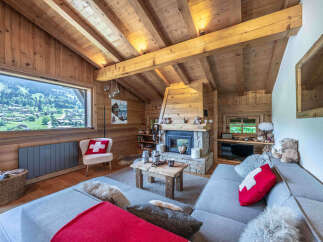 Experience the ultimate alpine retreat in this stunning wooden chalet, featuring a cozy living area with a stone fireplace and breathtaking mountain views through a large panoramic window.