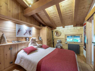 Experience cozy mountain living in this charming wooden bedroom, featuring a comfortable bed adorned with plush pillows and a warm red throw.