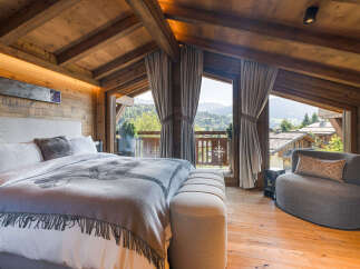 Experience luxury mountain living in this stunning chalet bedroom, featuring a plush king-sized bed adorned with a unique graphic blanket and a cozy upholstered bench.