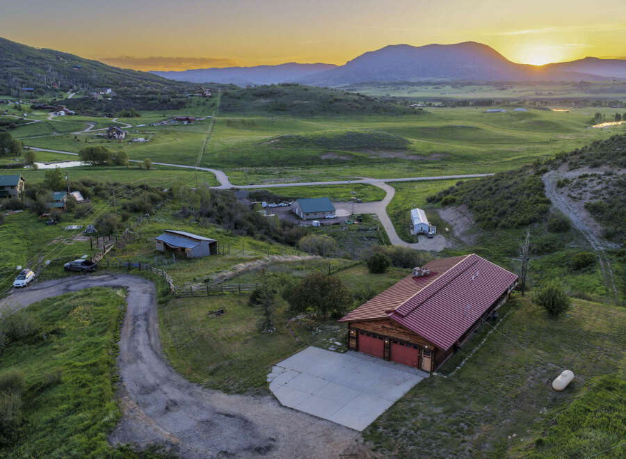 Experience serene mountain living with this stunning property featuring a spacious home with a vibrant red roof, nestled amidst rolling green hills.