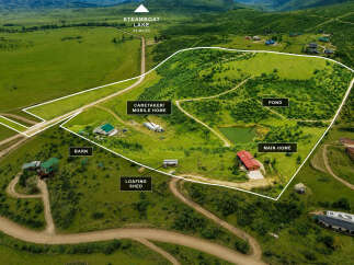 Discover this expansive property featuring a main home, caretaker's mobile home, and a barn, all nestled within a picturesque landscape.