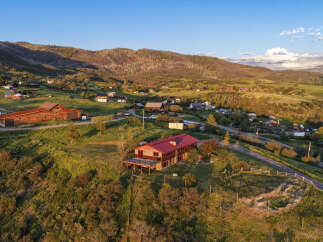Experience breathtaking mountain views from this stunning property, featuring a spacious wooden home with a vibrant red roof and expansive deck.