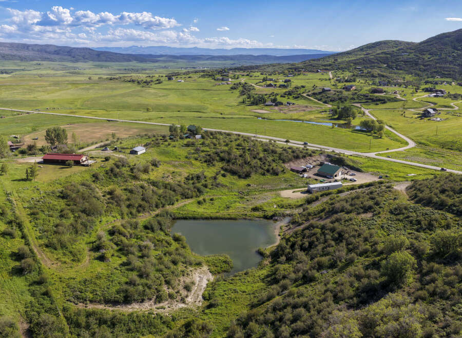 Discover this expansive rural property featuring a tranquil pond nestled amidst rolling green hills and lush vegetation.
