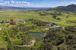 Discover this expansive rural property featuring a tranquil pond nestled amidst rolling green hills and lush vegetation.