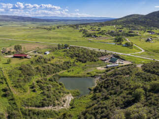 Discover this expansive rural property featuring a tranquil pond nestled amidst rolling green hills and lush vegetation.