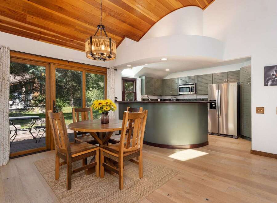 Enjoy meals with a view in this charming dining area, featuring a rustic wooden table and chairs set against a backdrop of lush greenery visible through large sliding glass doors.