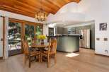 Enjoy meals with a view in this charming dining area, featuring a rustic wooden table and chairs set against a backdrop of lush greenery visible through large sliding glass doors.