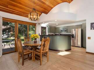 Enjoy meals with a view in this charming dining area, featuring a rustic wooden table and chairs set against a backdrop of lush greenery visible through large sliding glass doors.