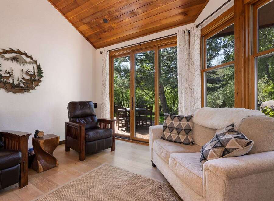 Experience rustic charm in this inviting living space featuring a vaulted wood-paneled ceiling and large sliding glass doors that open to a lush outdoor setting.