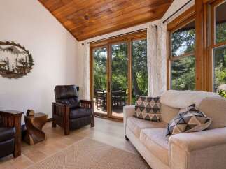 Experience rustic charm in this inviting living space featuring a vaulted wood-paneled ceiling and large sliding glass doors that open to a lush outdoor setting.