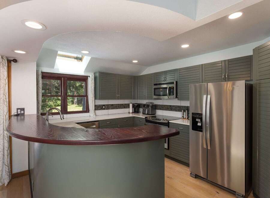 Discover this beautifully updated kitchen featuring sleek, gray shaker cabinets and a stunning curved, dark wood breakfast bar.