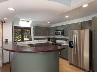 Discover this beautifully updated kitchen featuring sleek, gray shaker cabinets and a stunning curved, dark wood breakfast bar.